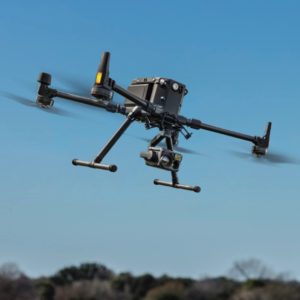 The image shows a drone captured mid-flight against a clear blue sky. The drone, featuring a sleek and modern design, hovers steadily, highlighting its advanced engineering and stability. The clean sky provides a vivid background, emphasizing the drone's presence and functionality. This photo showcases the drone in operation, symbolizing innovation and precision in aerial technology